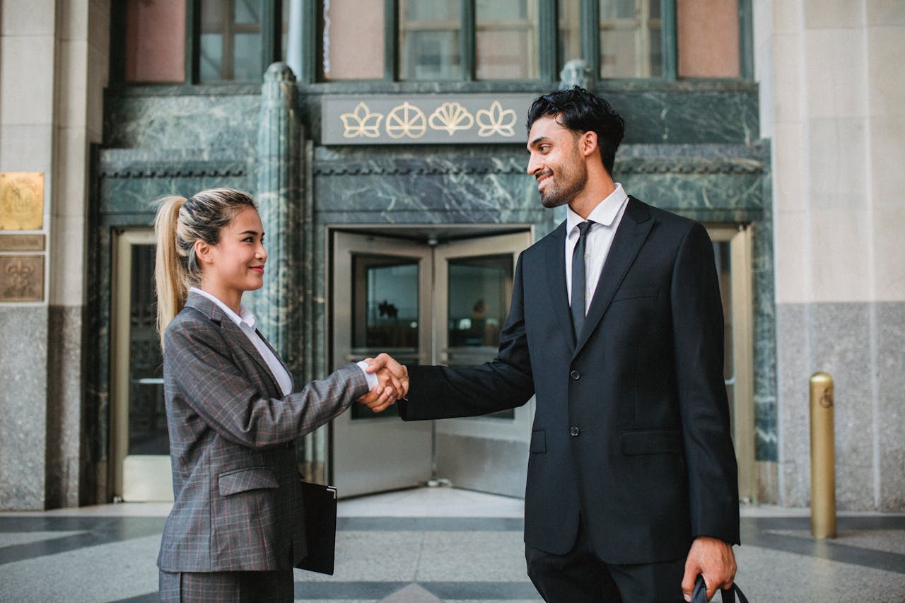 Two business professionals shaking hands outside a corporate building, symbolizing successful cooperation.